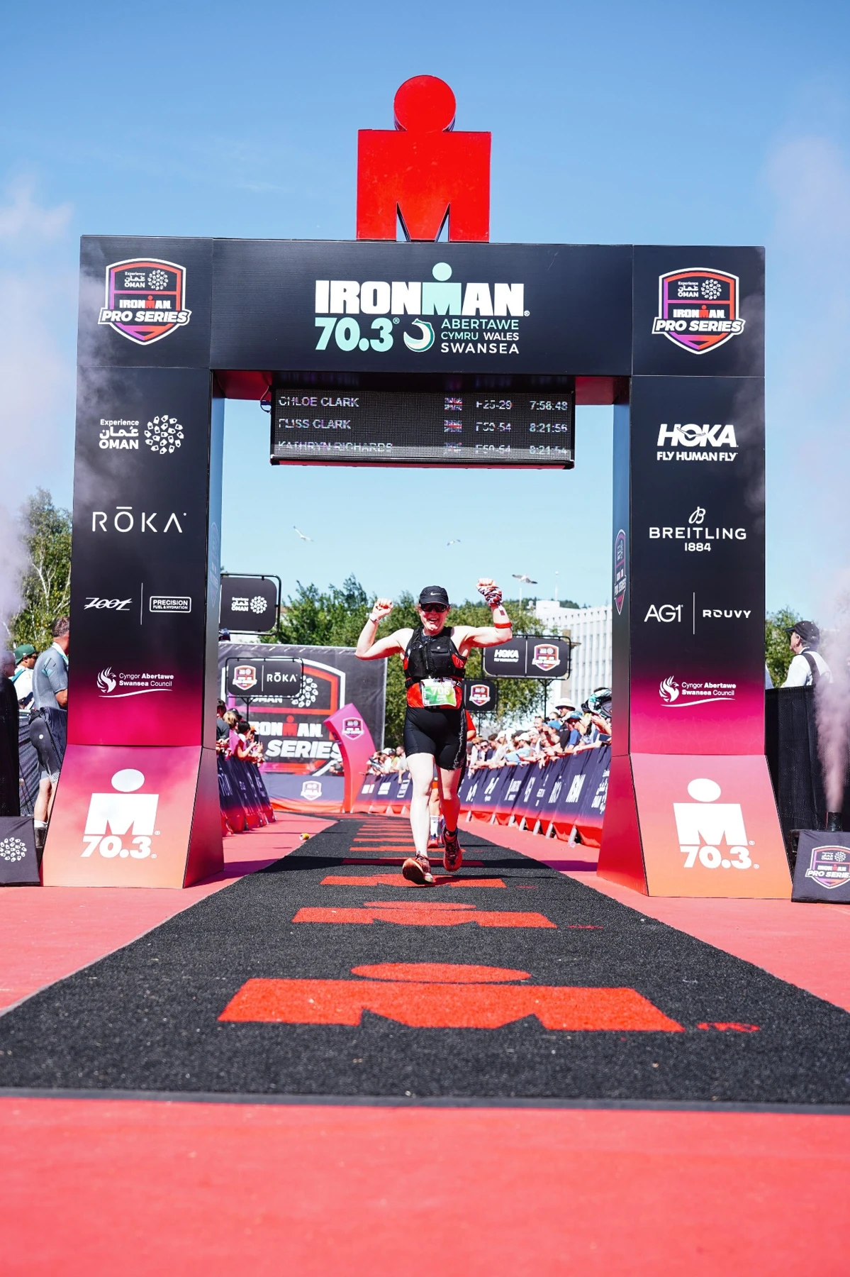 Fliss celebrating under the IRONMAN 70.3 Swansea finish arch